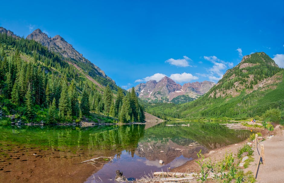 Stunning reflection of Maroon Bells in the tranquil lake under a vibrant blue sky in Colorado.