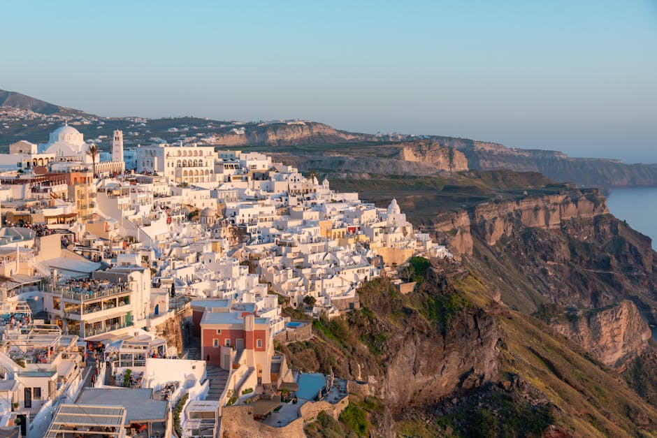 Spectacular aerial view of whitewashed buildings atop the cliffs of Santorini, Greece at sunset.
