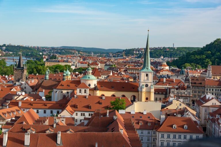 Aerial view of Prague showcasing red rooftops and historic landmarks under a clear blue sky.