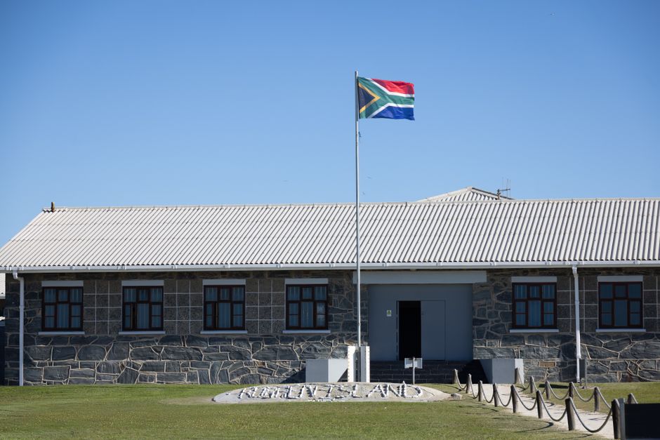 Robben Island Museum building with South African flag under clear blue sky.