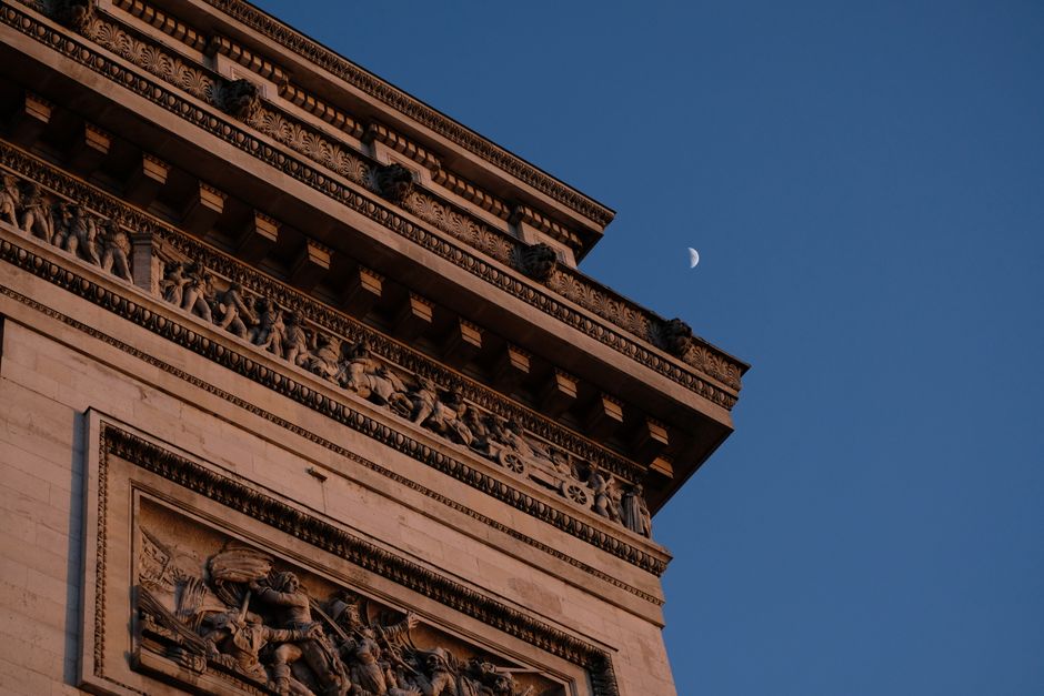 A detailed view of the Arc de Triomphe and a crescent moon set against a twilight sky in Paris, France.