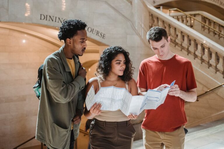 Focused young man pointing at map while searching for route with multiracial friends in Grand Central Terminal during trip in New York