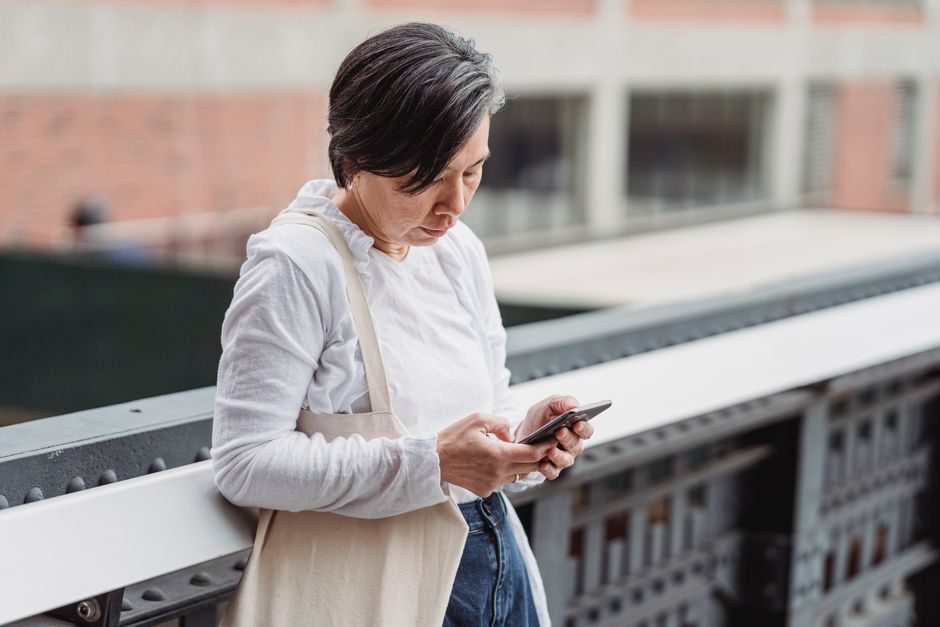 Casual scene of a woman interacting with her smartphone outdoors, leaning on railings.