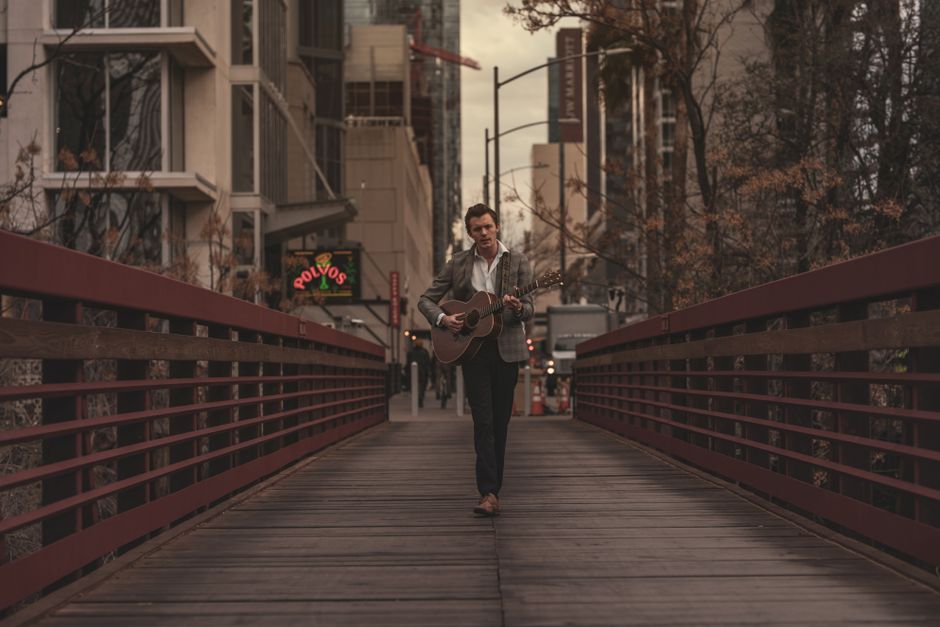 A man playing acoustic guitar on a city bridge at dusk, blending music with urban architecture.