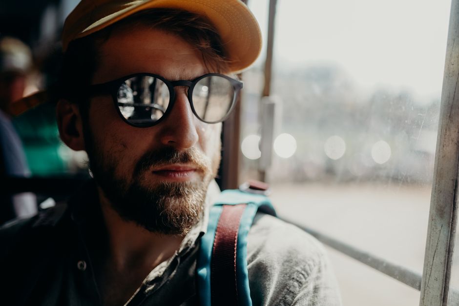 A bearded man in sunglasses and hat gazes out a bus window, capturing the essence of travel and exploration.
