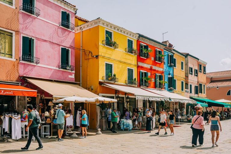 Busy market scene with colorful buildings in Burano, Italy, bustling with shoppers.