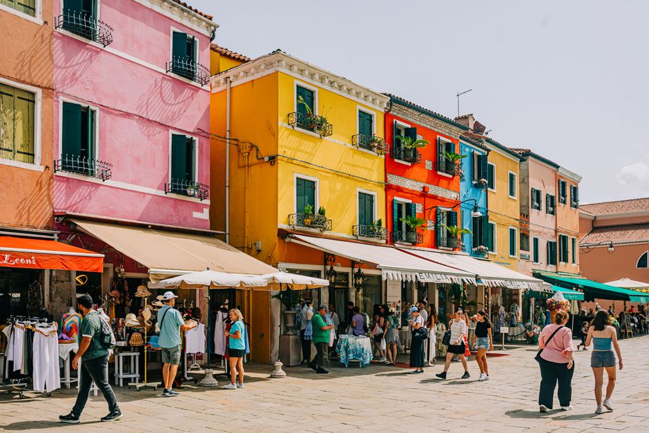 Busy market scene with colorful buildings in Burano, Italy, bustling with shoppers.