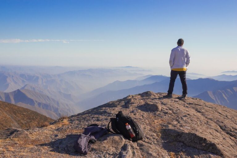 A man stands on a mountain in Peru, overlooking the Andes with a backpack nearby, capturing adventure and wanderlust.