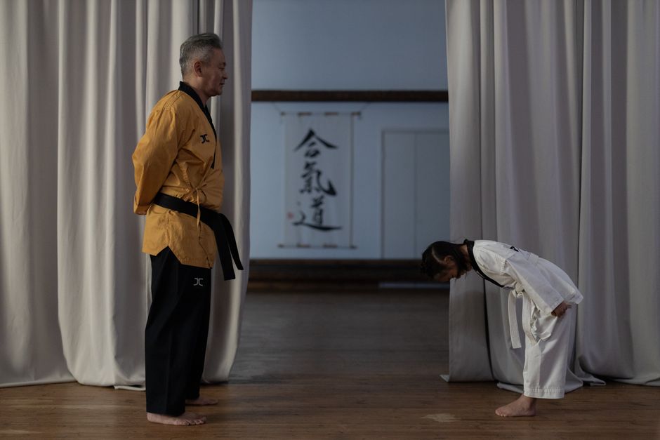Sensei and child in martial arts class demonstrating respect through bowing in a dojo setting.