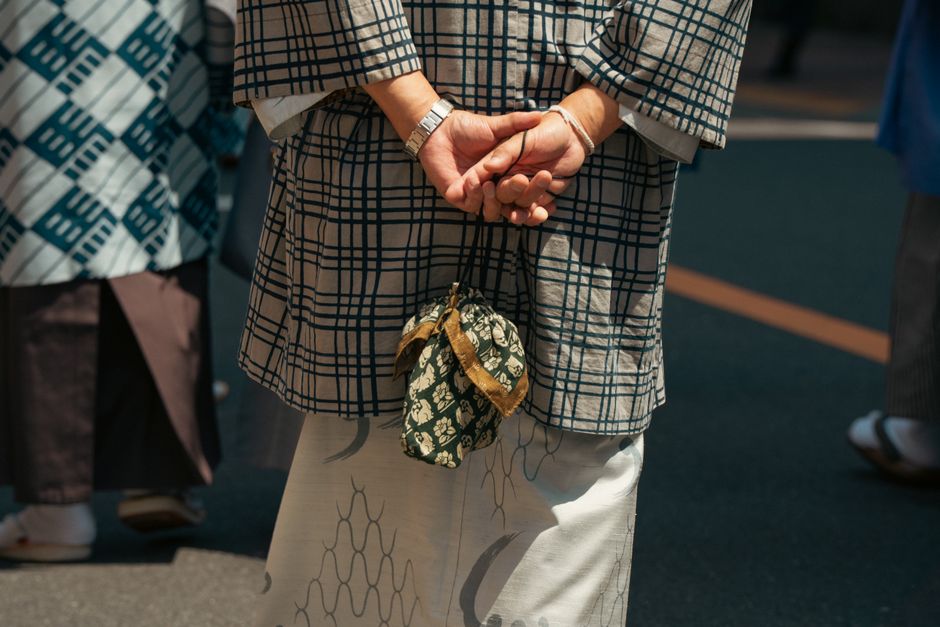 Person in traditional Japanese kimono standing on a Tokyo street, hands clasped behind back.