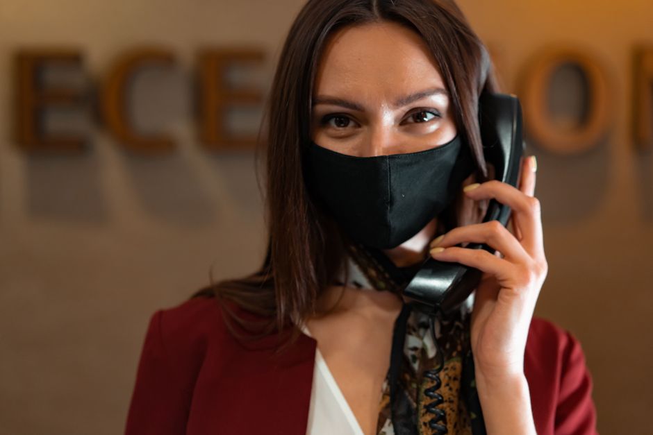 Professional woman receptionist wearing a mask while talking on the phone at the reception desk.