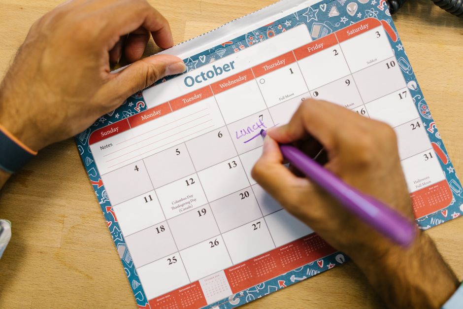 Close-up of a person writing reminder on an October calendar with a purple pen.