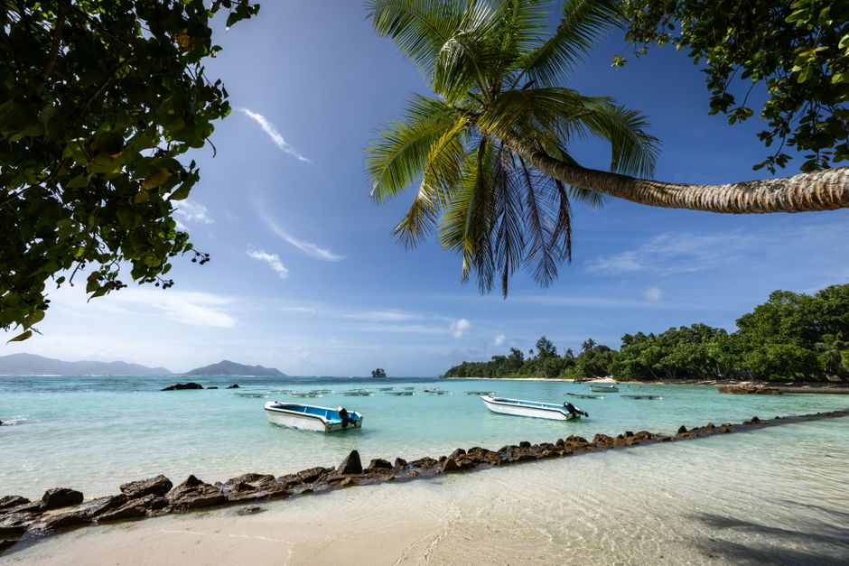 Serene tropical beach in Seychelles with clear waters, boats, and lush palm trees.