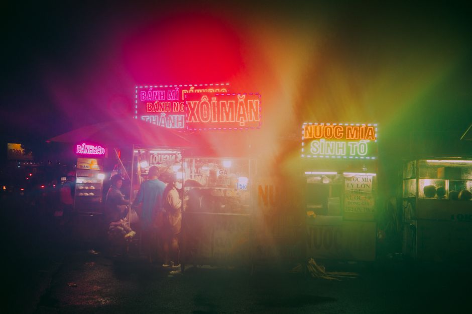 Neon-lit street food stalls create a vibrant atmosphere at a bustling night market.