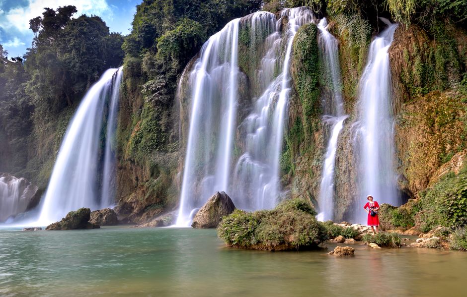 A majestic waterfall with a woman in traditional clothes standing on the rocks. Ideal for nature and travel imagery.