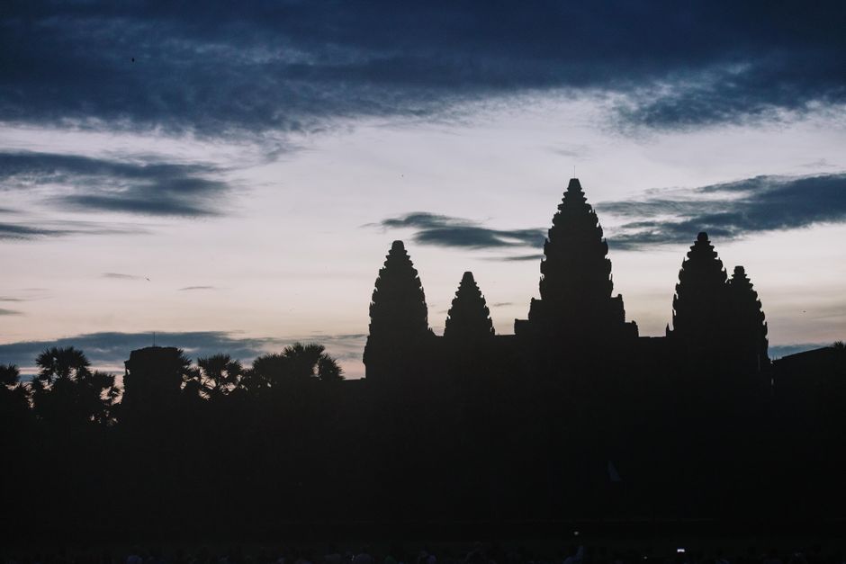 Silhouette of Angkor Wat temple at dusk with dramatic sky.