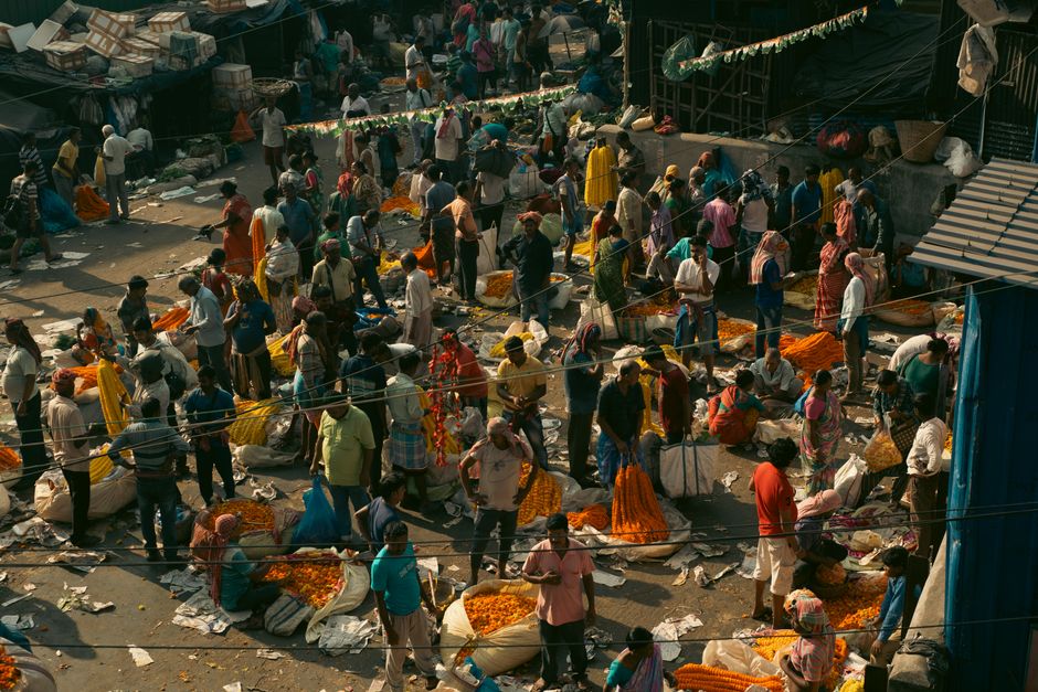 A bustling outdoor market scene with people buying and selling vibrant orange flowers.