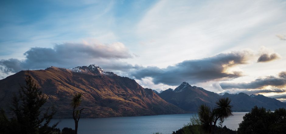 Breathtaking view of Lake Wakatipu against the backdrop of majestic mountains under a cloudy sky.
