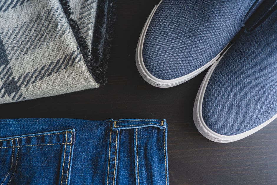 Flat lay of denim jeans, blue sneakers, and a plaid scarf for a casual look.