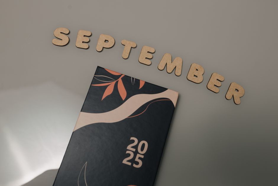 Flat lay of a calendar with September spelled in wooden letters on a neutral background.