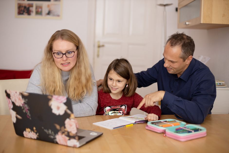 A family is engaged in homeschooling, using technology to learn together in a cozy home setting.